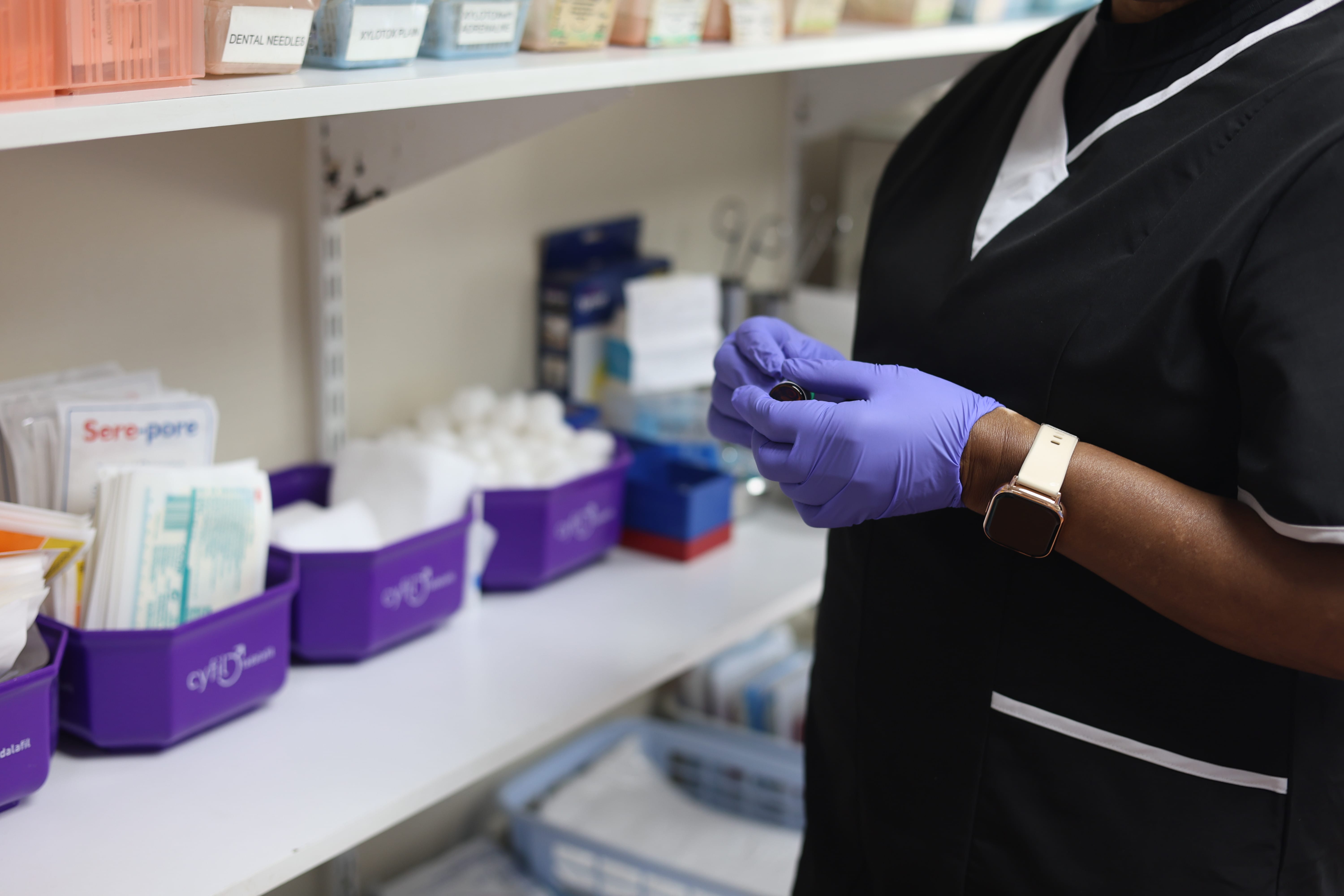 A gloved team member beside shelves of medical supplies at Sunningdale Medical Centre