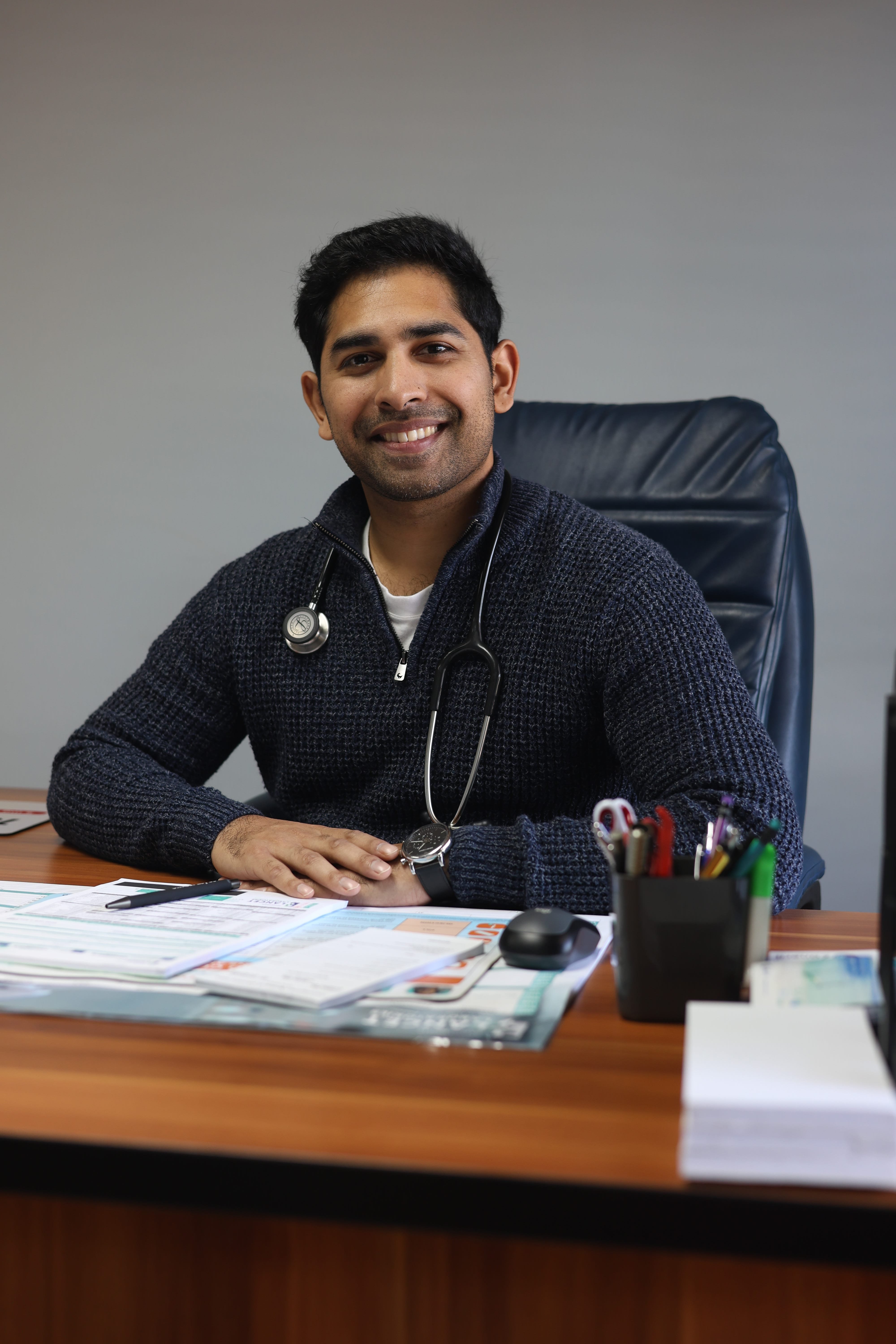 A doctor smiling at a desk in a Sunningdale Medical Centre consulting room