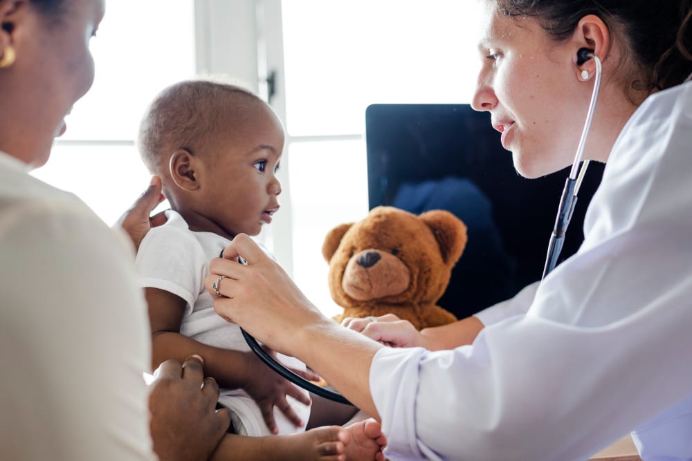 A doctor listening to a baby's chest with a stethoscope while a parent holds the child